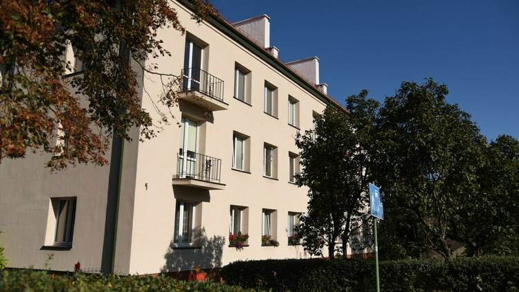 Starej&scaron;i trinadstropni stanovanjski blok s svetlo fasado in balkoni med drevesi